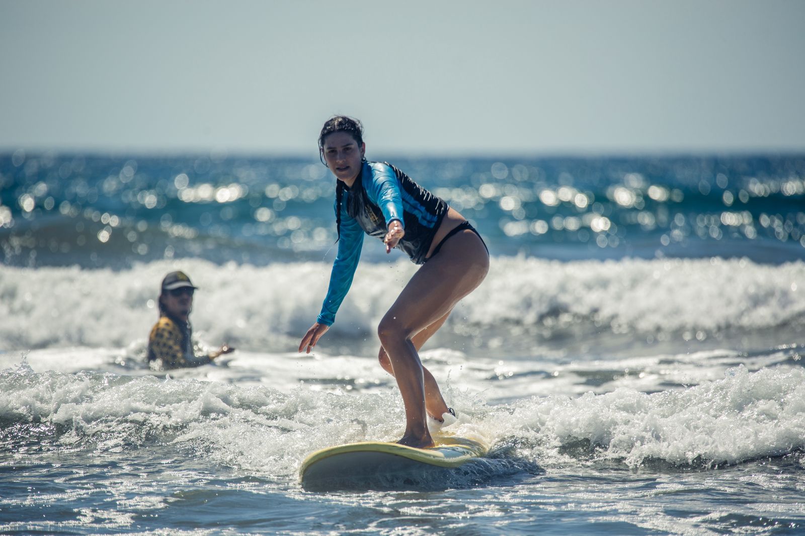 Student riding a wave on a soft-top longboard in Nosara